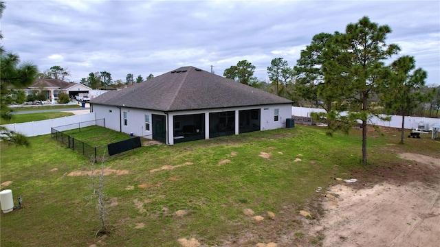 rear view of house with roof with shingles, stucco siding, a lawn, a sunroom, and a fenced backyard