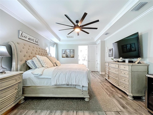 bedroom with a raised ceiling, visible vents, crown molding, and wood finished floors