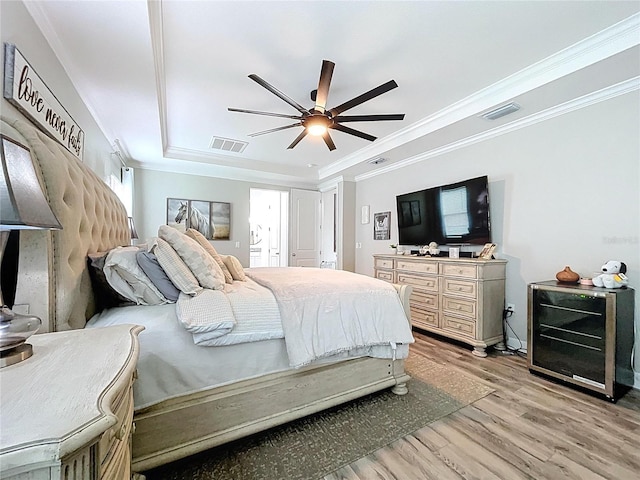 bedroom featuring light wood-type flooring, visible vents, a raised ceiling, and crown molding