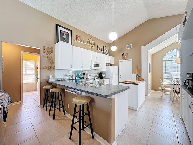 kitchen featuring light tile patterned floors, white appliances, dark countertops, and a peninsula