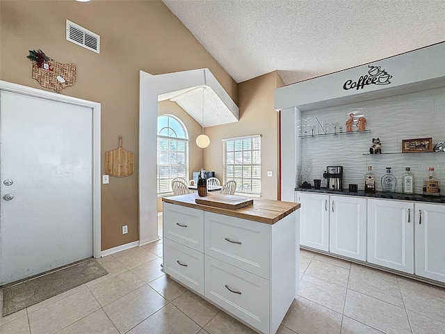 kitchen with light tile patterned floors, visible vents, wooden counters, lofted ceiling, and white cabinetry