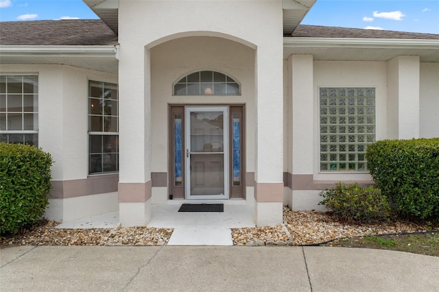 property entrance featuring stucco siding and a shingled roof