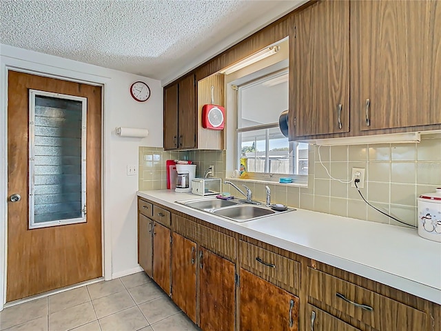 kitchen with light tile patterned floors, backsplash, light countertops, a textured ceiling, and a sink