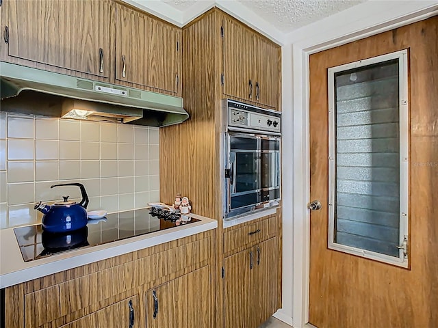 kitchen with under cabinet range hood, light countertops, a textured ceiling, black appliances, and backsplash