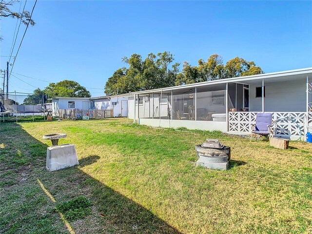 view of yard featuring a trampoline, fence, and a sunroom