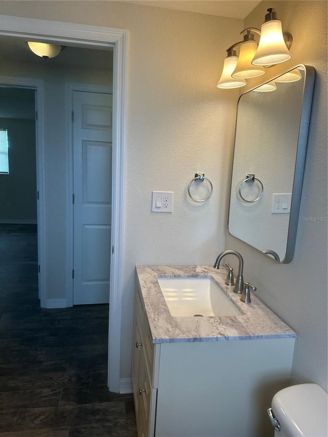 half bathroom featuring vanity, toilet, wood finished floors, and baseboards