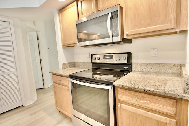 kitchen featuring light brown cabinets, light stone counters, stainless steel appliances, light wood-style floors, and baseboards