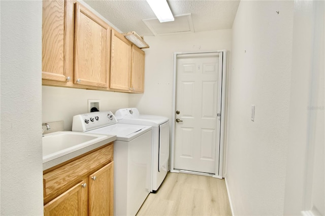 washroom with light wood finished floors, cabinet space, a sink, a textured ceiling, and washing machine and dryer