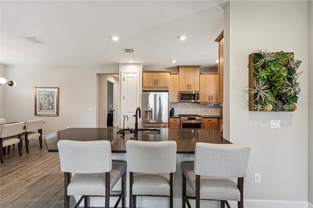 kitchen featuring a breakfast bar area, dark countertops, visible vents, a sink, and high quality appliances