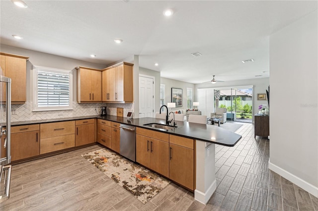 kitchen with tasteful backsplash, dark countertops, a peninsula, a sink, and stainless steel dishwasher