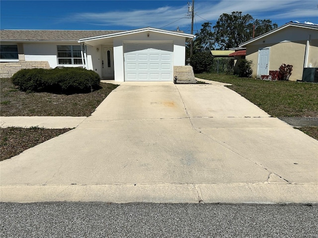 view of front facade featuring a garage, driveway, central air condition unit, and stucco siding