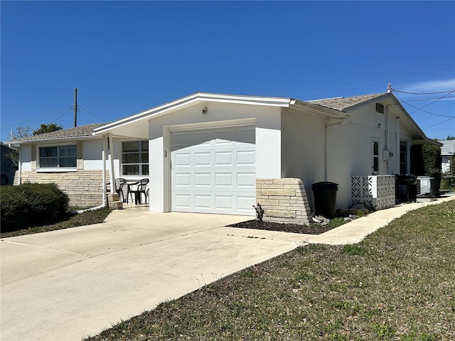 view of side of property featuring central AC unit, concrete driveway, stone siding, an attached garage, and stucco siding