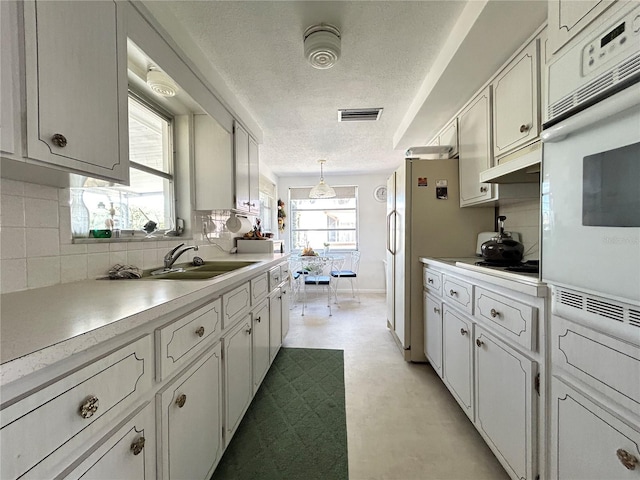 kitchen with light floors, light countertops, backsplash, a sink, and under cabinet range hood