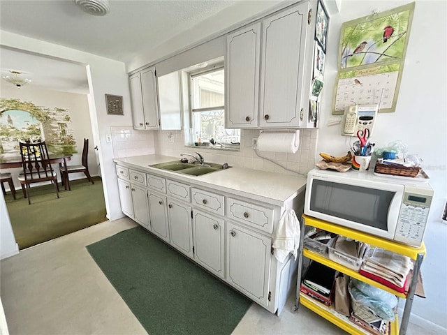 kitchen with white microwave, a sink, visible vents, light countertops, and backsplash