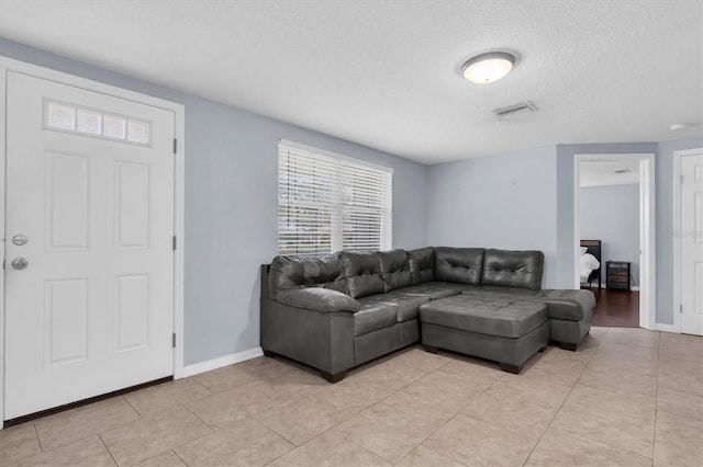 living area featuring light tile patterned floors, visible vents, baseboards, and a textured ceiling