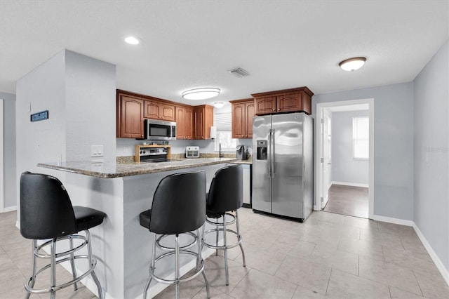 kitchen featuring visible vents, a peninsula, plenty of natural light, stainless steel appliances, and a kitchen bar