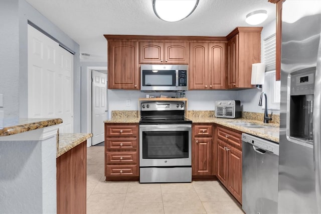 kitchen featuring a sink, a textured ceiling, stainless steel appliances, light tile patterned floors, and light stone countertops