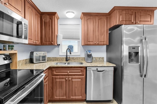 kitchen with a sink, light stone counters, appliances with stainless steel finishes, and brown cabinets