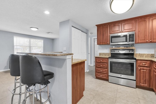 kitchen featuring a breakfast bar, light tile patterned floors, stainless steel appliances, and light stone countertops