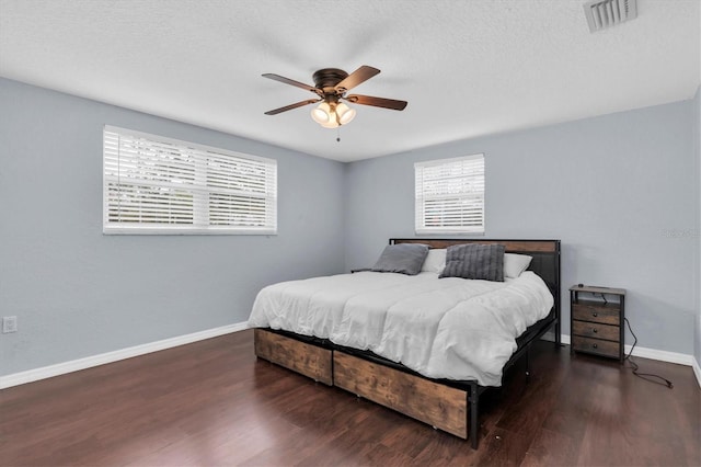 bedroom with a textured ceiling, wood finished floors, visible vents, and baseboards