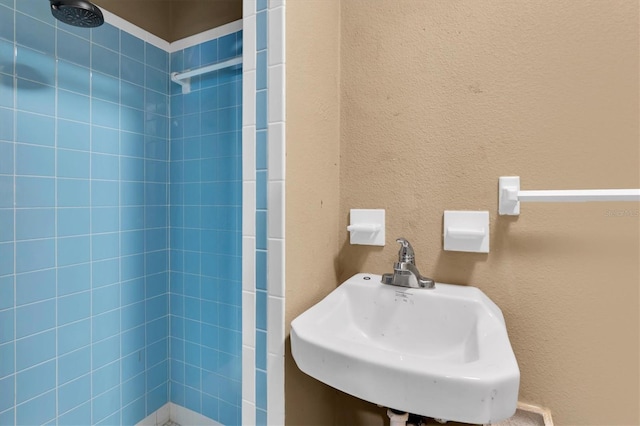 bathroom with a tile shower, a textured wall, and a sink