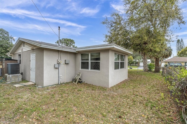 rear view of house featuring stucco siding, a yard, central AC unit, and fence