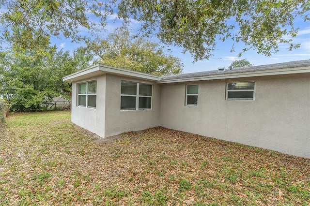 view of property exterior with stucco siding, a lawn, and fence