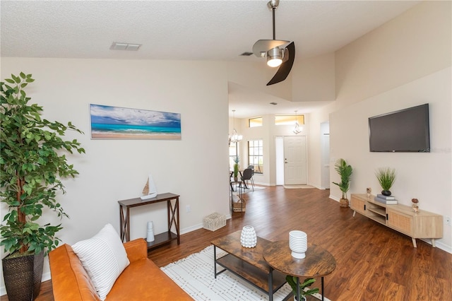 living area featuring lofted ceiling, visible vents, a textured ceiling, wood finished floors, and baseboards