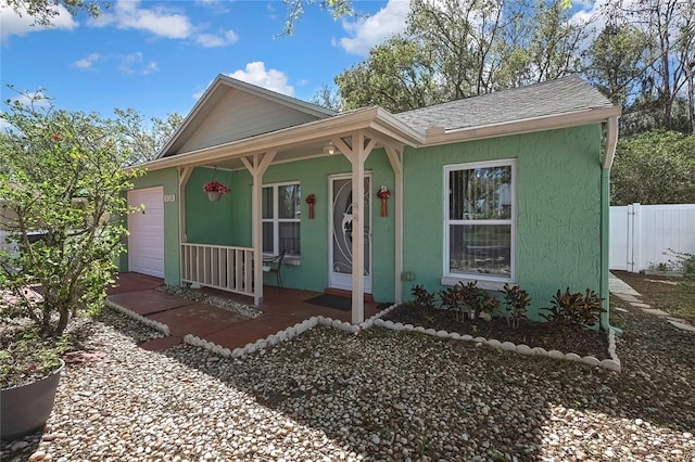 view of front facade featuring a porch, a garage, fence, roof with shingles, and stucco siding