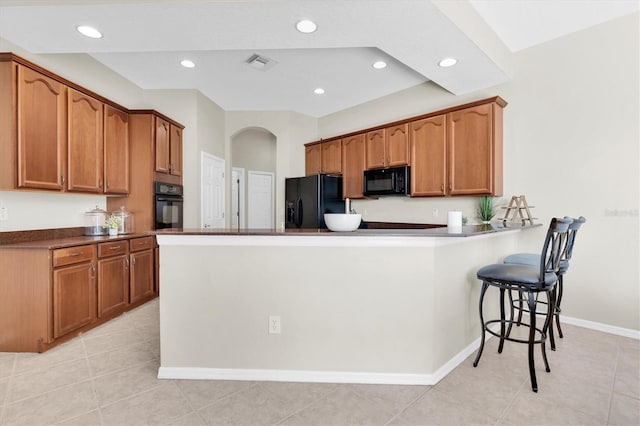 kitchen with visible vents, a kitchen bar, a peninsula, brown cabinetry, and black appliances