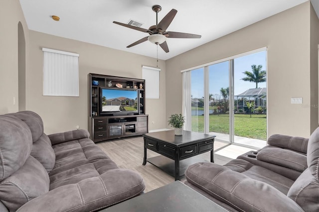 living room with light wood-style flooring, arched walkways, visible vents, and ceiling fan