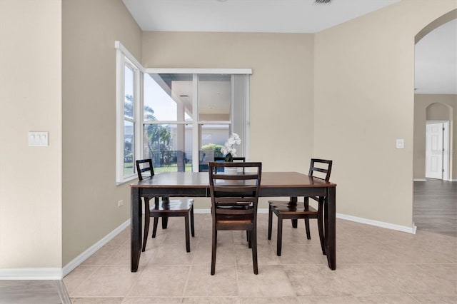 dining space featuring light tile patterned floors, baseboards, and arched walkways