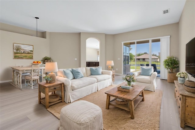 living area featuring arched walkways, light wood-style floors, visible vents, and baseboards