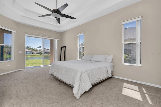 bedroom with access to exterior, a tray ceiling, carpet floors, baseboards, and ceiling fan