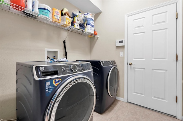 washroom featuring washer and dryer, laundry area, light tile patterned floors, and baseboards