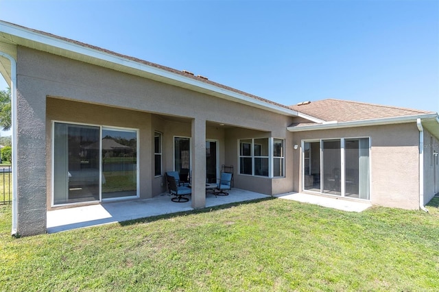 rear view of property featuring a patio area, a lawn, and stucco siding