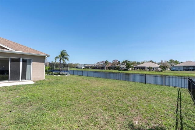 view of yard with a fenced backyard, a residential view, a trampoline, and a water view