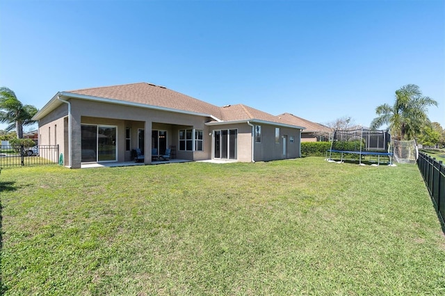 back of house with a fenced backyard, stucco siding, a yard, and a trampoline