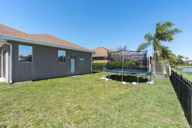 view of yard with a trampoline, fence, and a water view