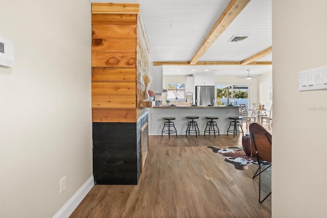 interior space featuring beam ceiling, visible vents, freestanding refrigerator, wood finished floors, and baseboards