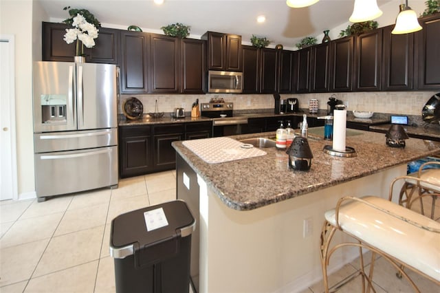 kitchen featuring light tile patterned floors, a breakfast bar, appliances with stainless steel finishes, decorative backsplash, and dark stone countertops