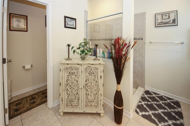 bathroom featuring tile patterned flooring, a tile shower, and baseboards