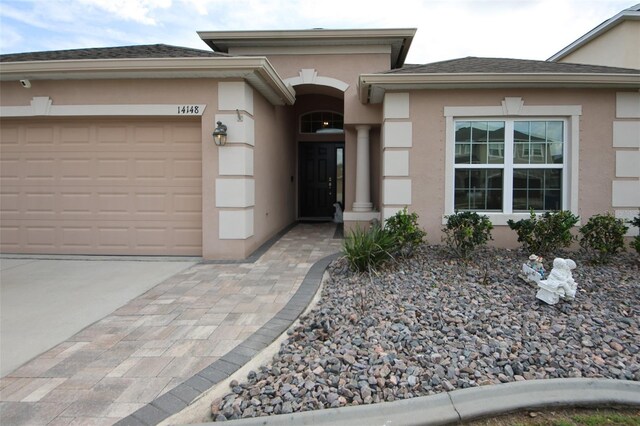 doorway to property featuring an attached garage, driveway, a shingled roof, and stucco siding