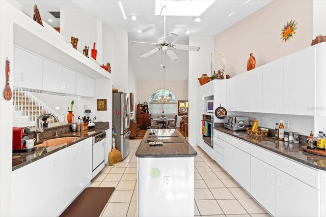 kitchen with light tile patterned floors, a kitchen island, stainless steel appliances, high vaulted ceiling, and a sink