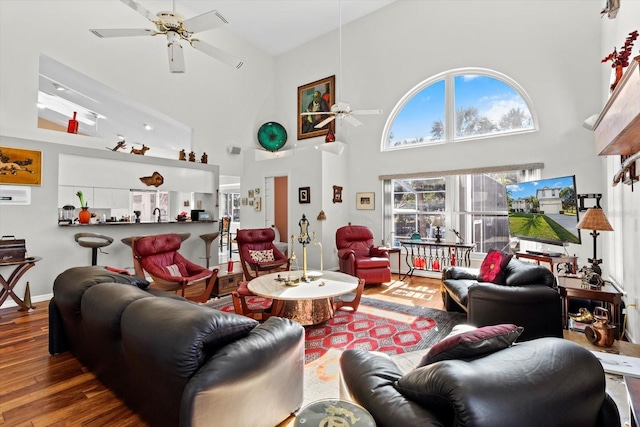 living room with a ceiling fan, a towering ceiling, baseboards, and wood finished floors