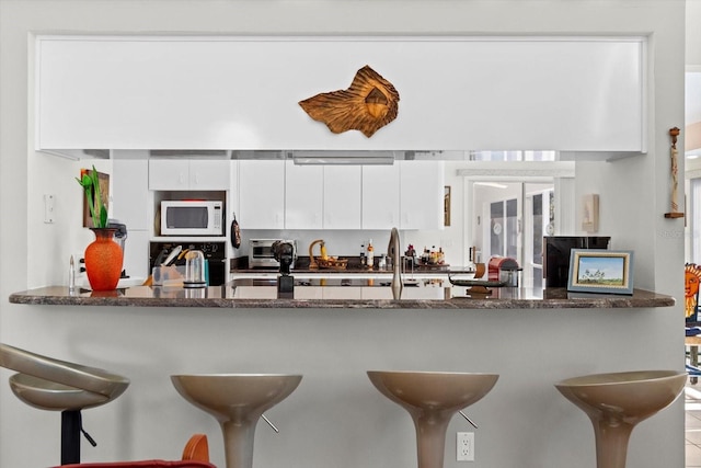 kitchen with dark stone counters, a peninsula, a breakfast bar area, and white microwave