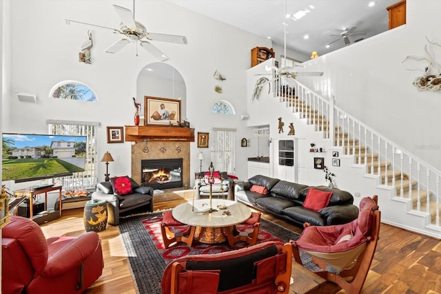 living room featuring ceiling fan, stairway, a tiled fireplace, and wood finished floors