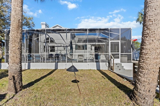 rear view of house featuring glass enclosure, a lawn, and a chimney