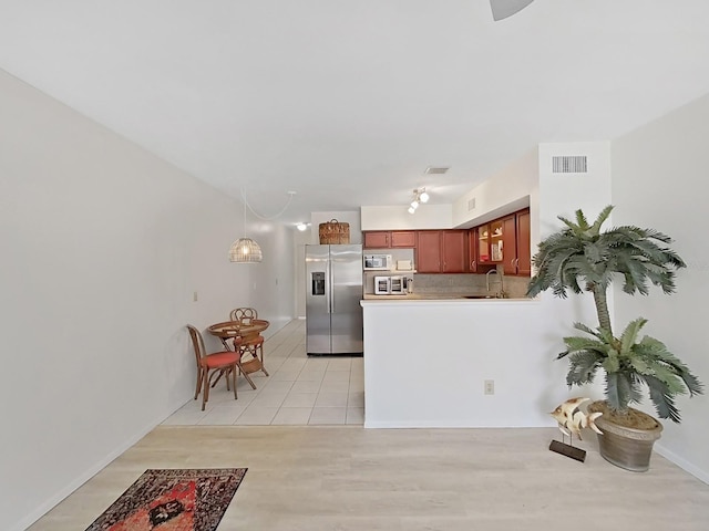 kitchen with light wood-style flooring, a peninsula, a sink, visible vents, and appliances with stainless steel finishes