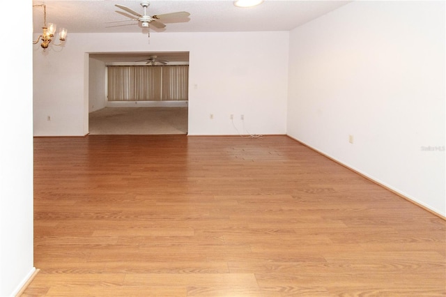 unfurnished room featuring ceiling fan with notable chandelier and light wood-style floors